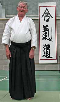 Foster Sensei standing in front of
                                Aikido kanji